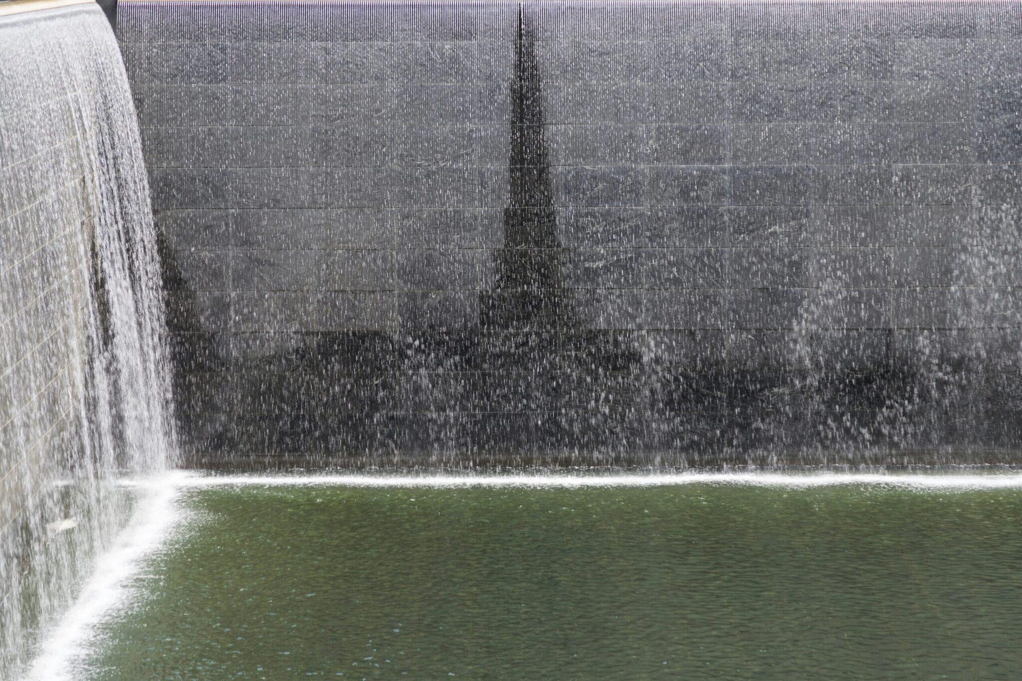 A monumental waterfall cascading from a concrete structure into a sunken reflecting pool framed by greenery