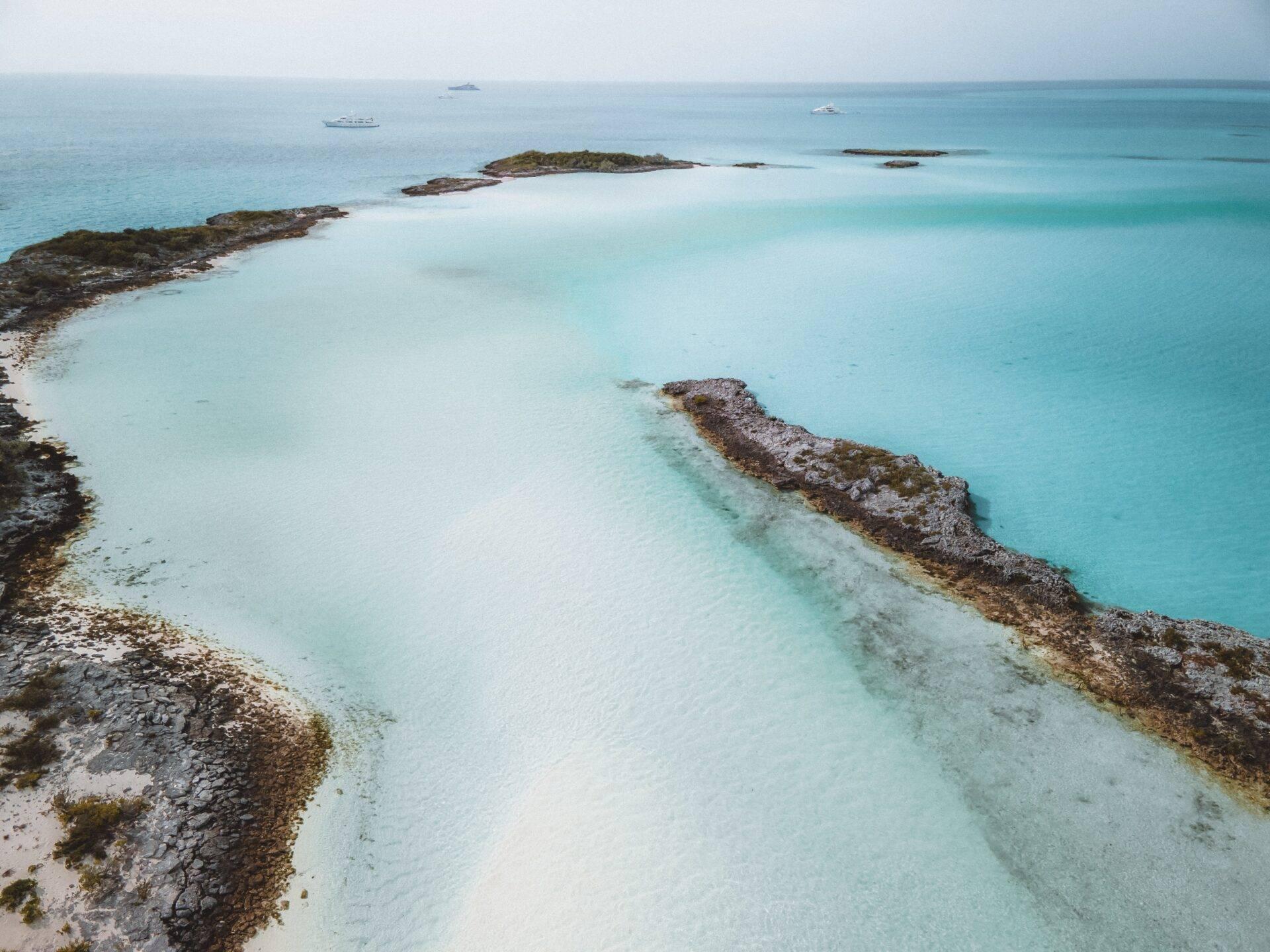Aerial view of a turquoise lagoon in the Bahamas with rocky islets and boats anchored offshore