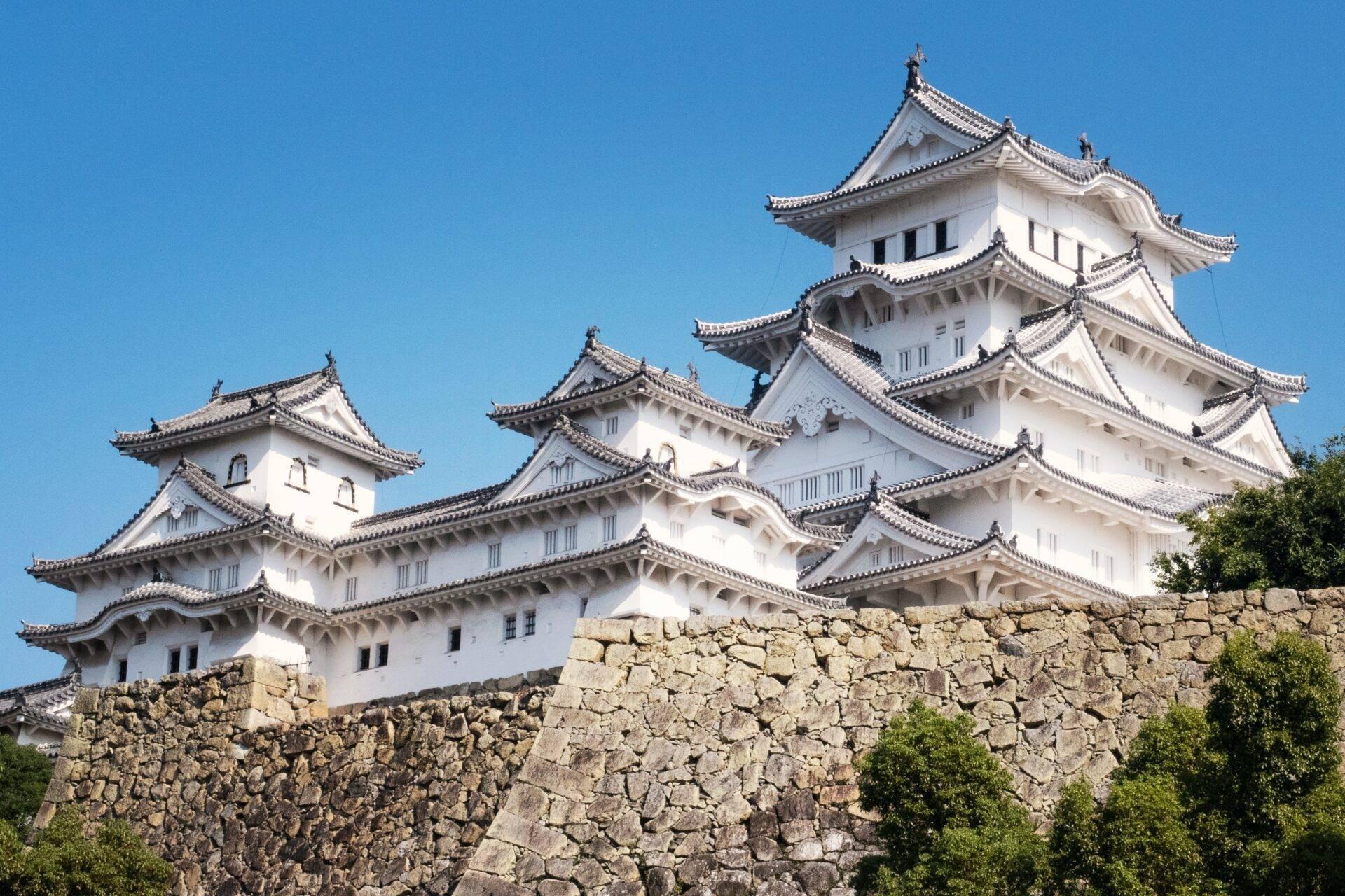 Eine weiße japanische Burg mit geschwungenen Dächern und schwarzen Ziegeln auf einer Steinmauer unter blauem Himmel