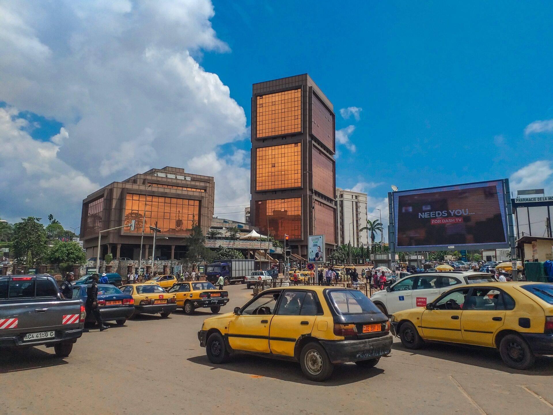 Una plaza urbana animada con taxis amarillos y edificios modernos de fachadas naranjas bajo un cielo azul