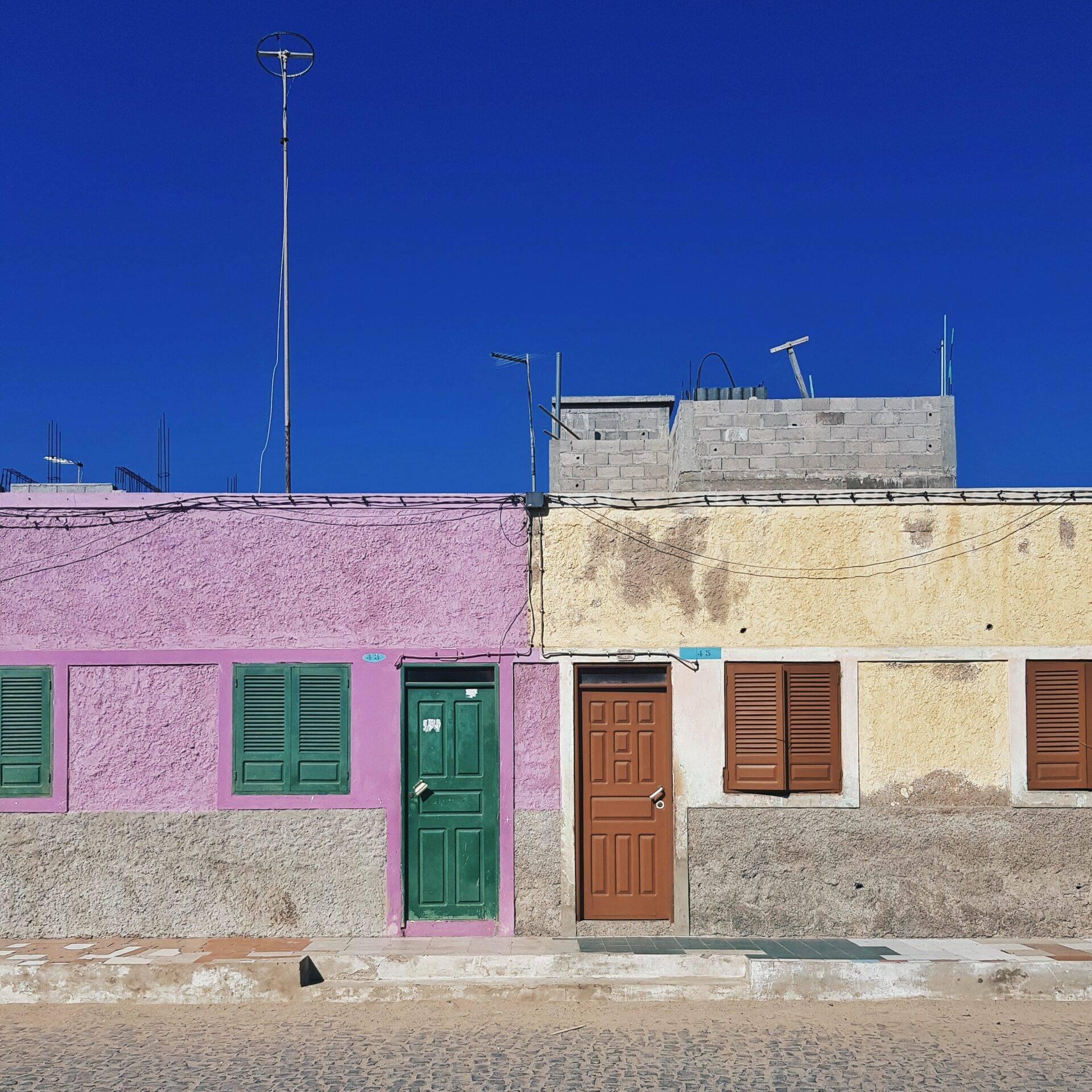 Colourful facade of pink and beige houses with green and brown doors under an intense blue sky