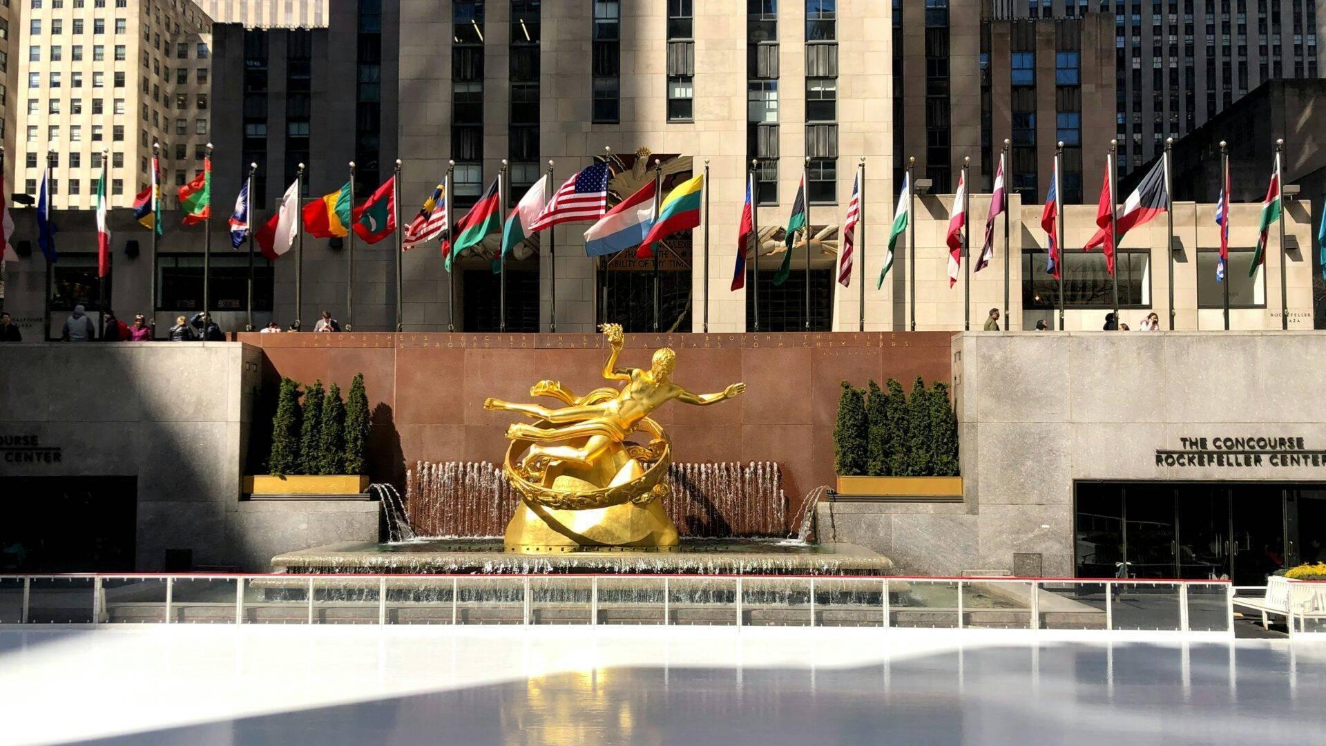 Piazza pubblica con statua dorata, bandiere internazionali e pista di pattinaggio sul ghiaccio in inverno a New York