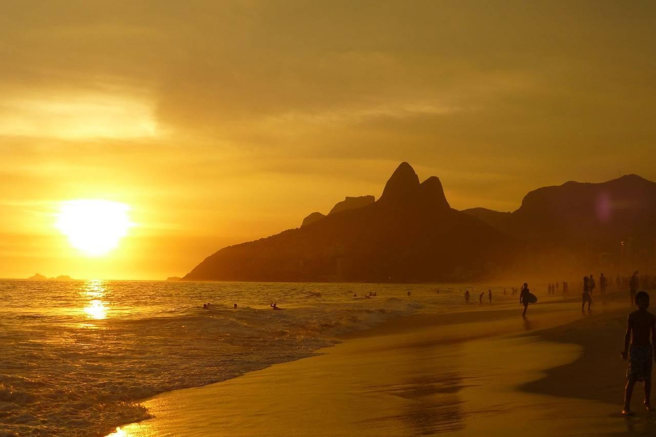 Goldener Sonnenuntergang über einem brasilianischen Strand mit Felsberg und Badegästen