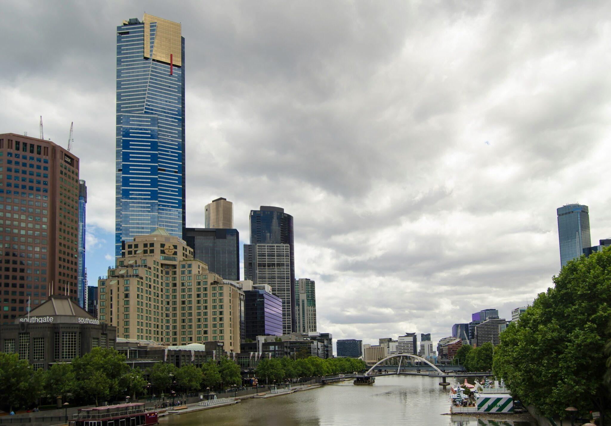 Skyline urbano con rascacielos modernos, río y puente en arco, árboles verdes y cielo nublado