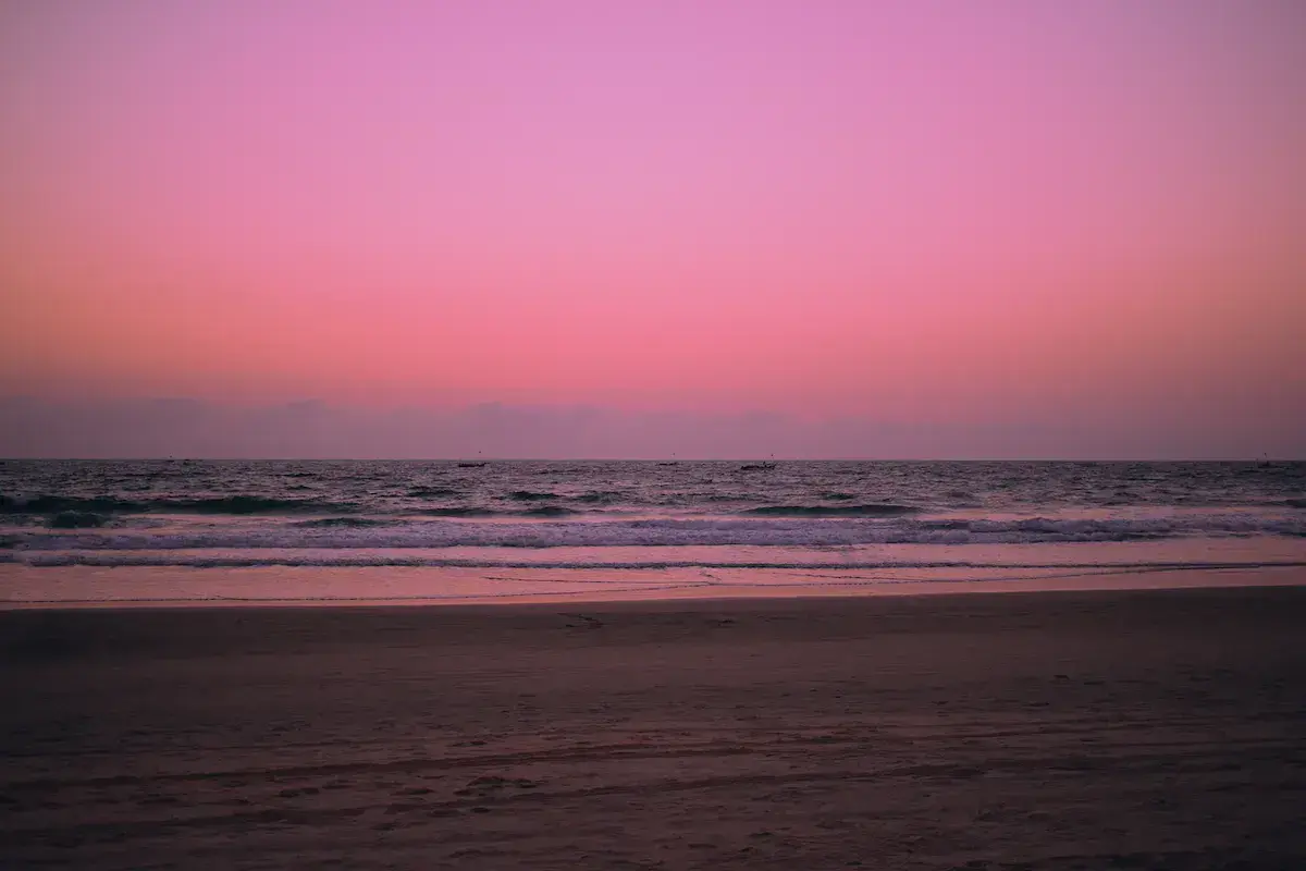 Atardecer o amanecer rosado sobre una playa desierta con olas rompientes y un cielo en degradado