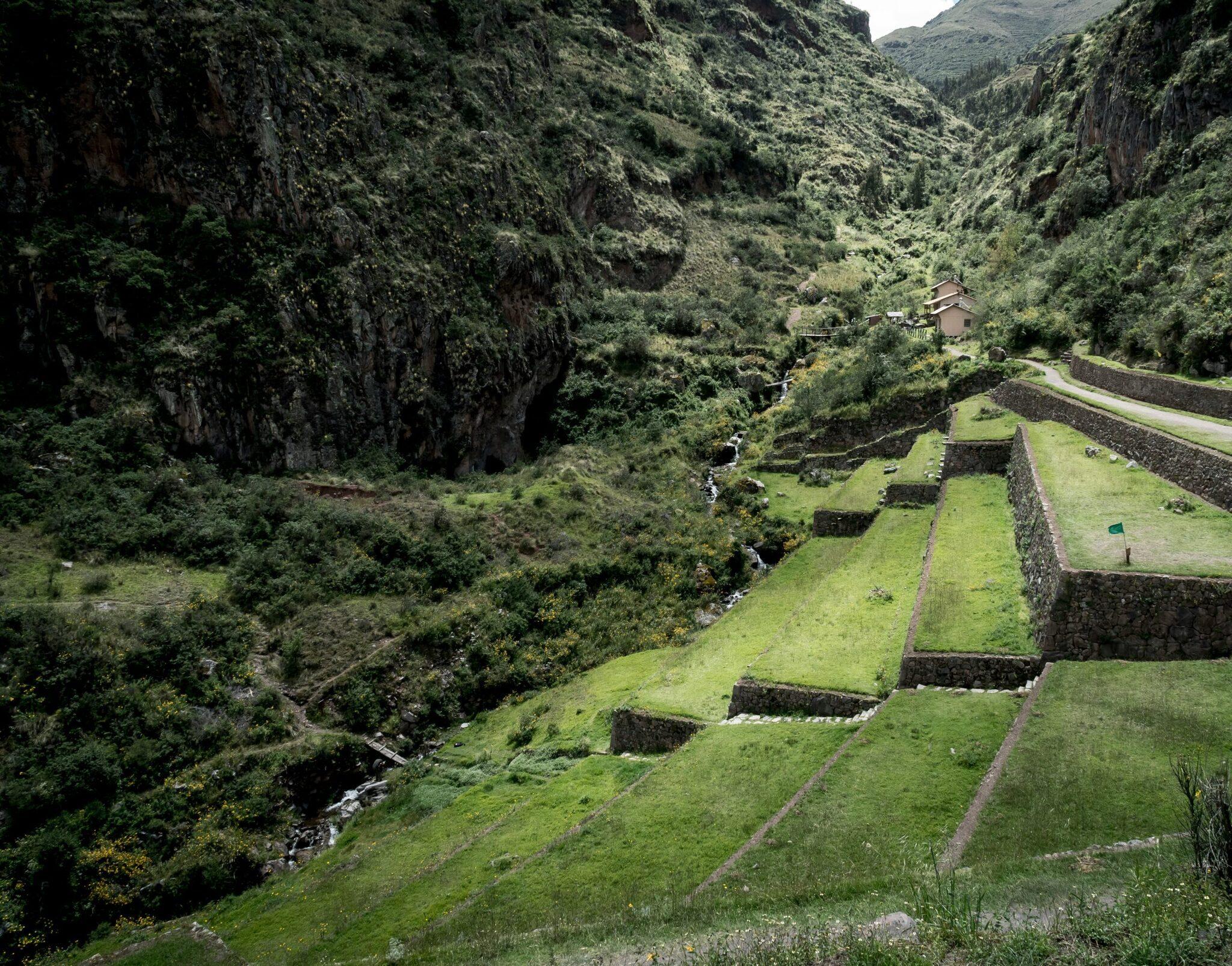 Ruines incas en terrasses dans une vallée montagneuse verdoyante avec bâtiment colonial en arrière-plan