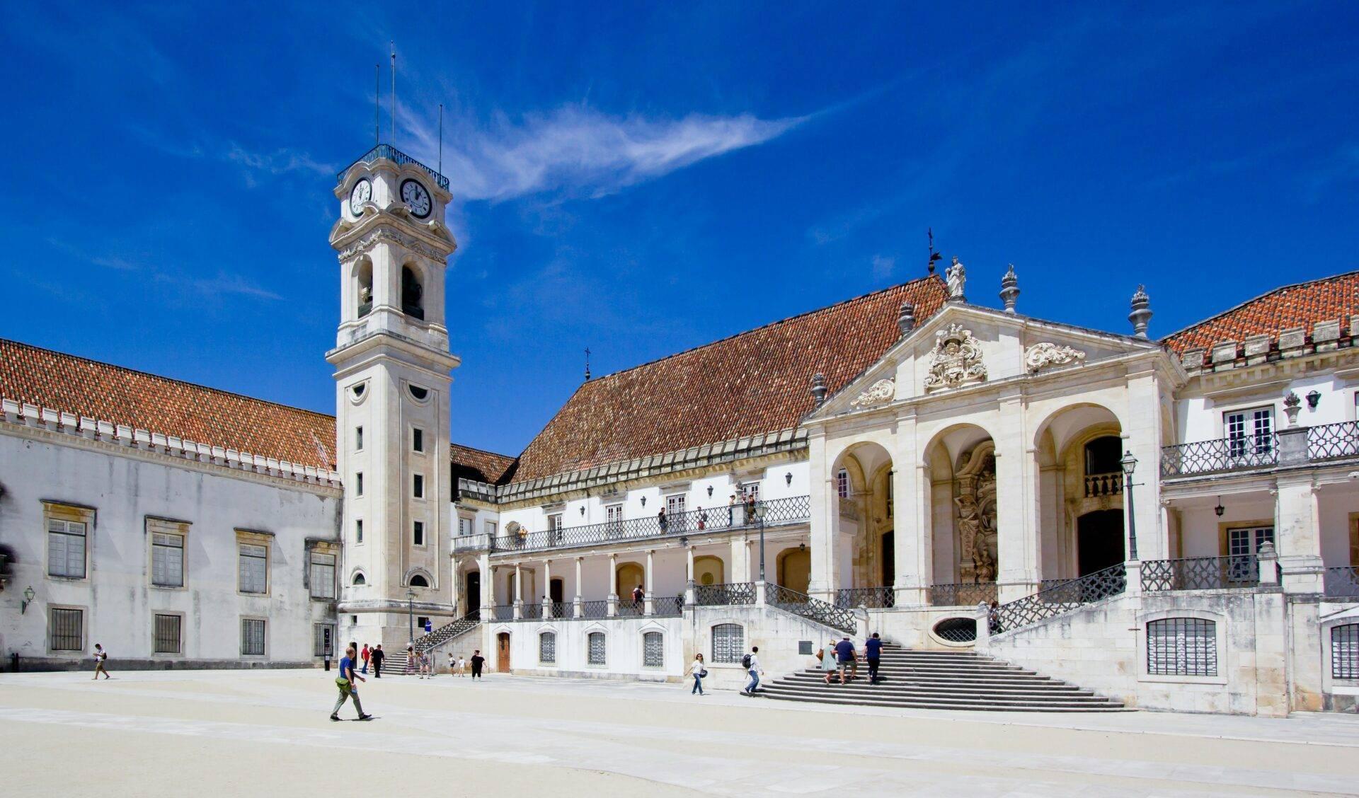 Innenhof einer historischen Universität mit weißem Glockenturm, Kolonialgebäuden und Azulejo-Kacheln unter blauem Himmel