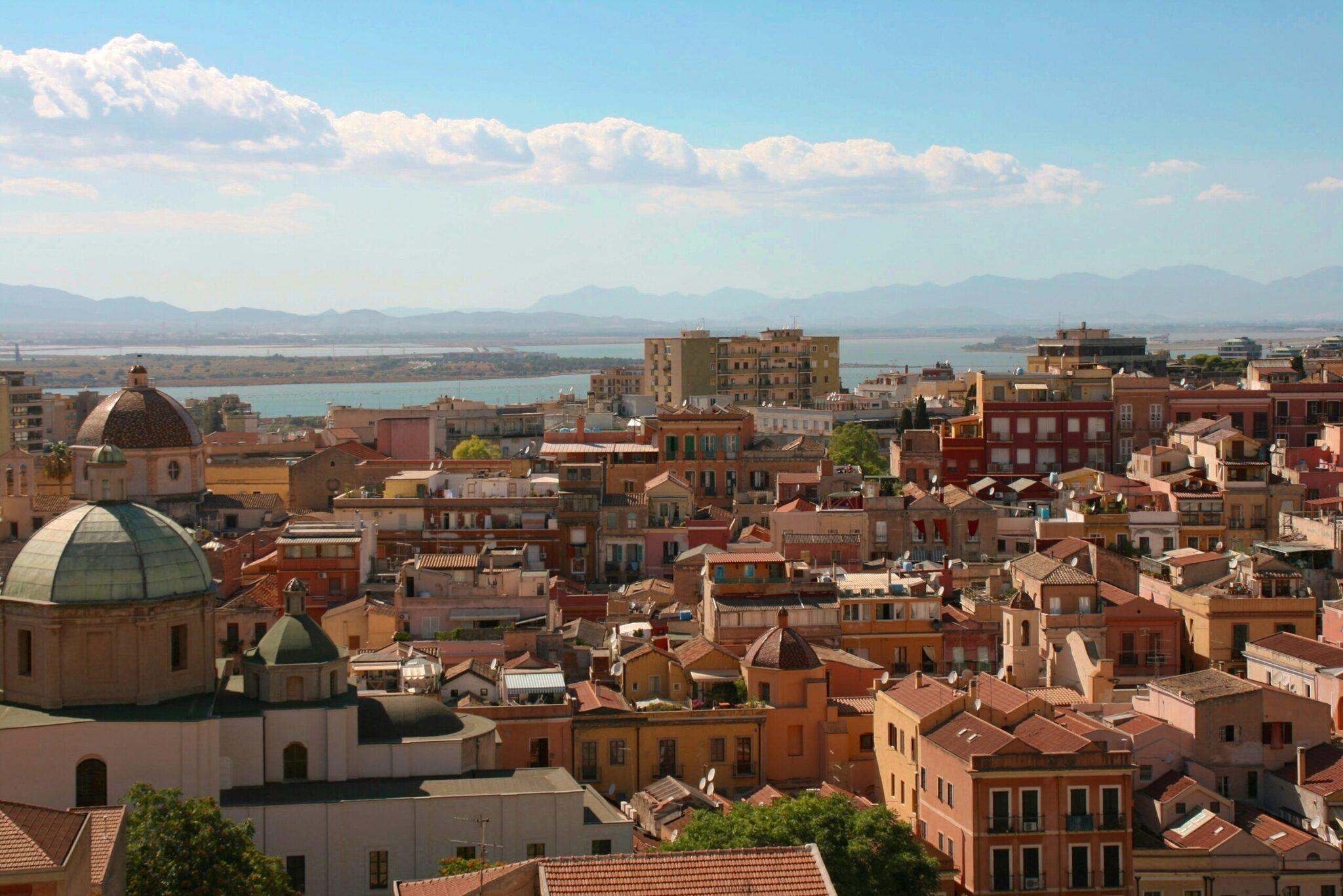 Vista panorámica de una ciudad costera mediterránea con iglesia de cúpula, arquitectura colorida y mar turquesa al fondo