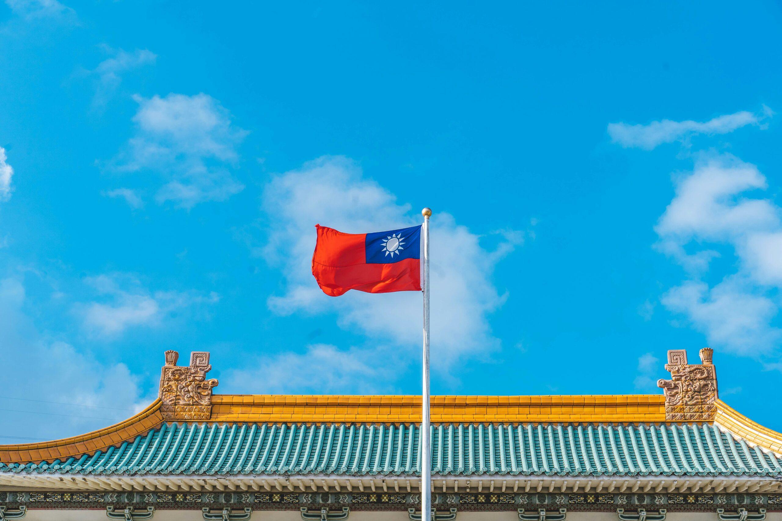 La bandera de Taiwán ondea frente a un templo tradicional con tejados dorados y turquesas bajo un cielo azul