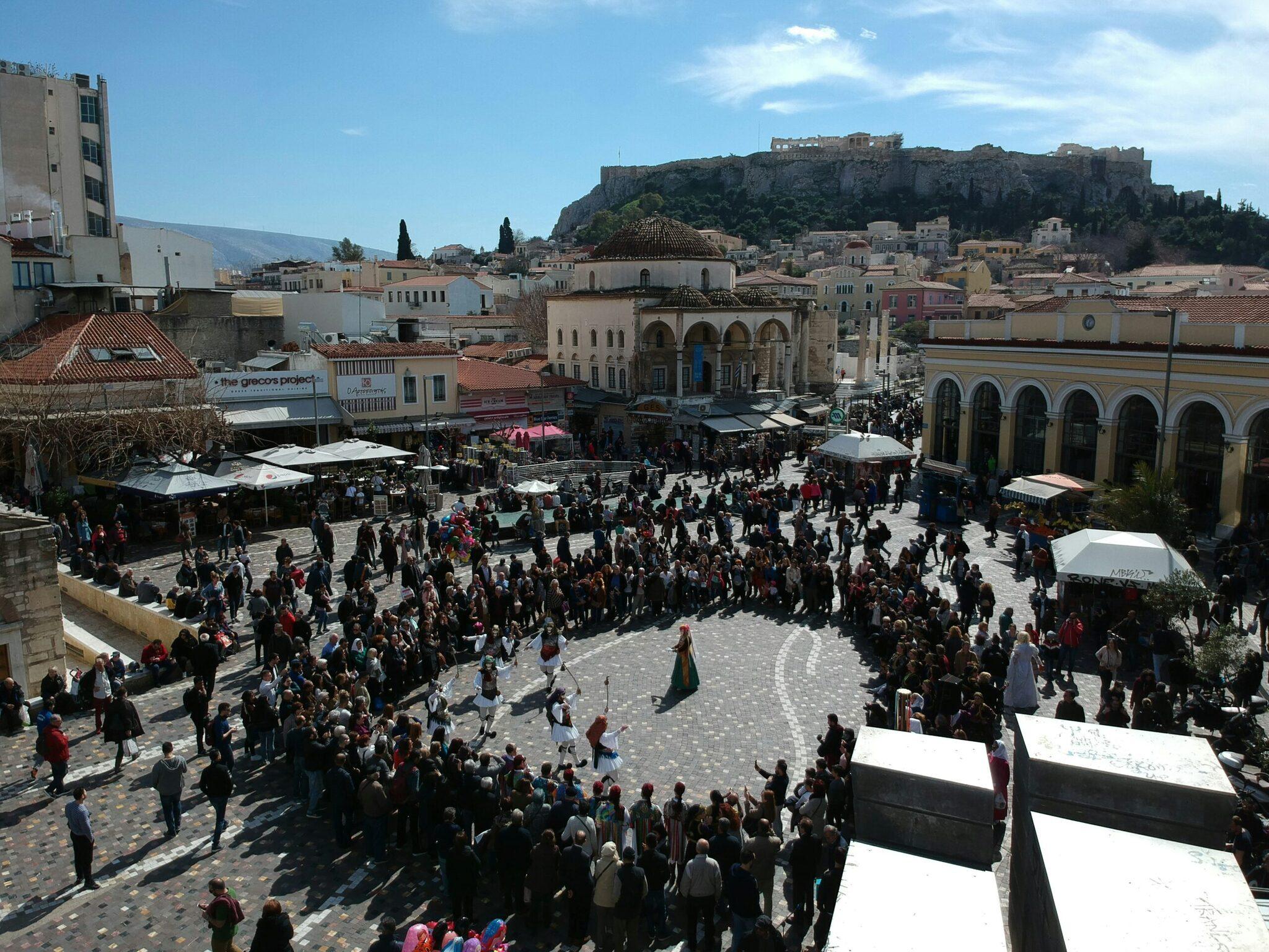 Ein belebter Platz mit Touristenmassen, historischen Gebäuden und der Akropolis im Hintergrund