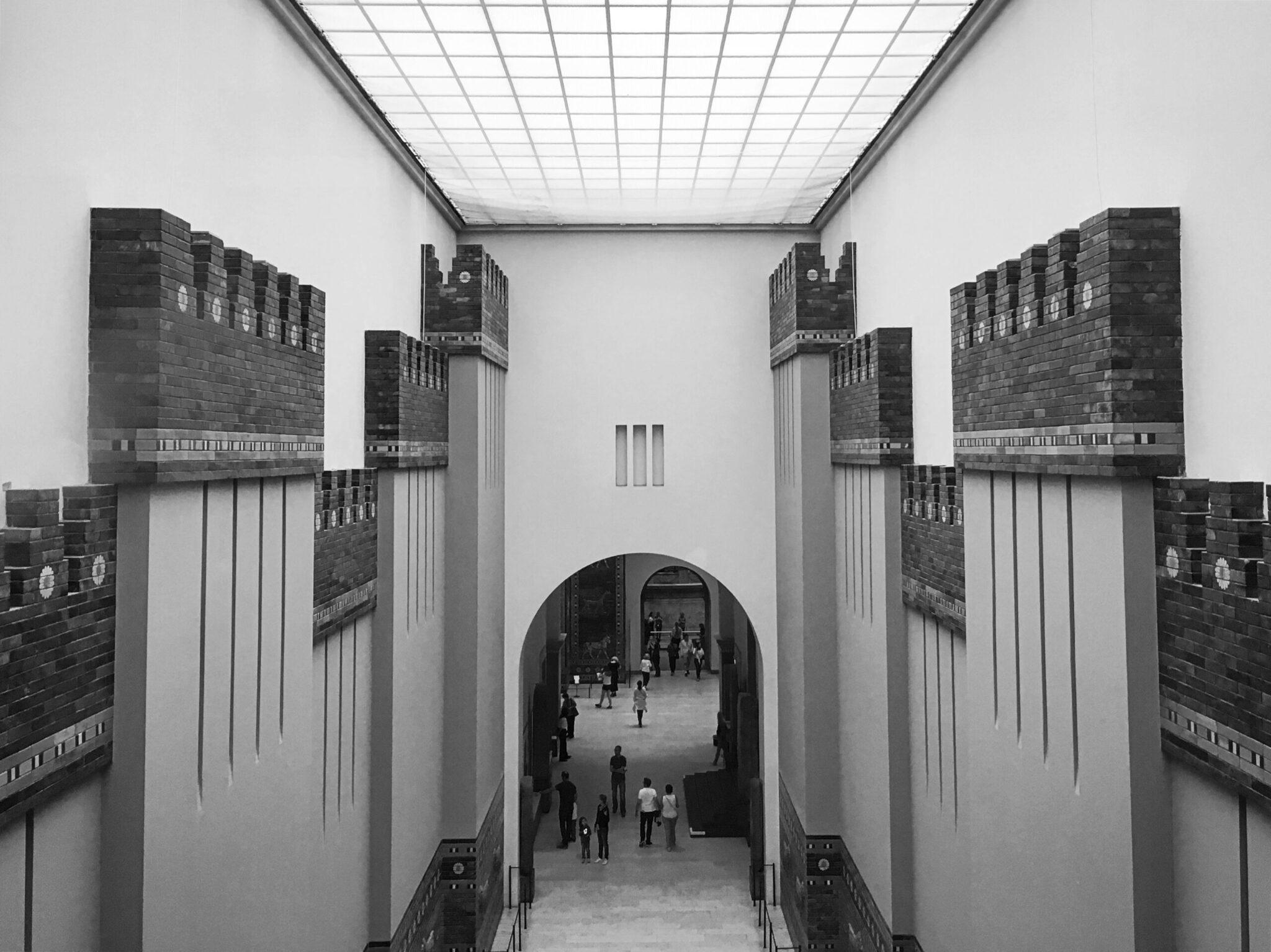 Reconstrucción arquitectónica de una puerta de ciudad antigua con torres macizas y visitantes cruzando el arco central