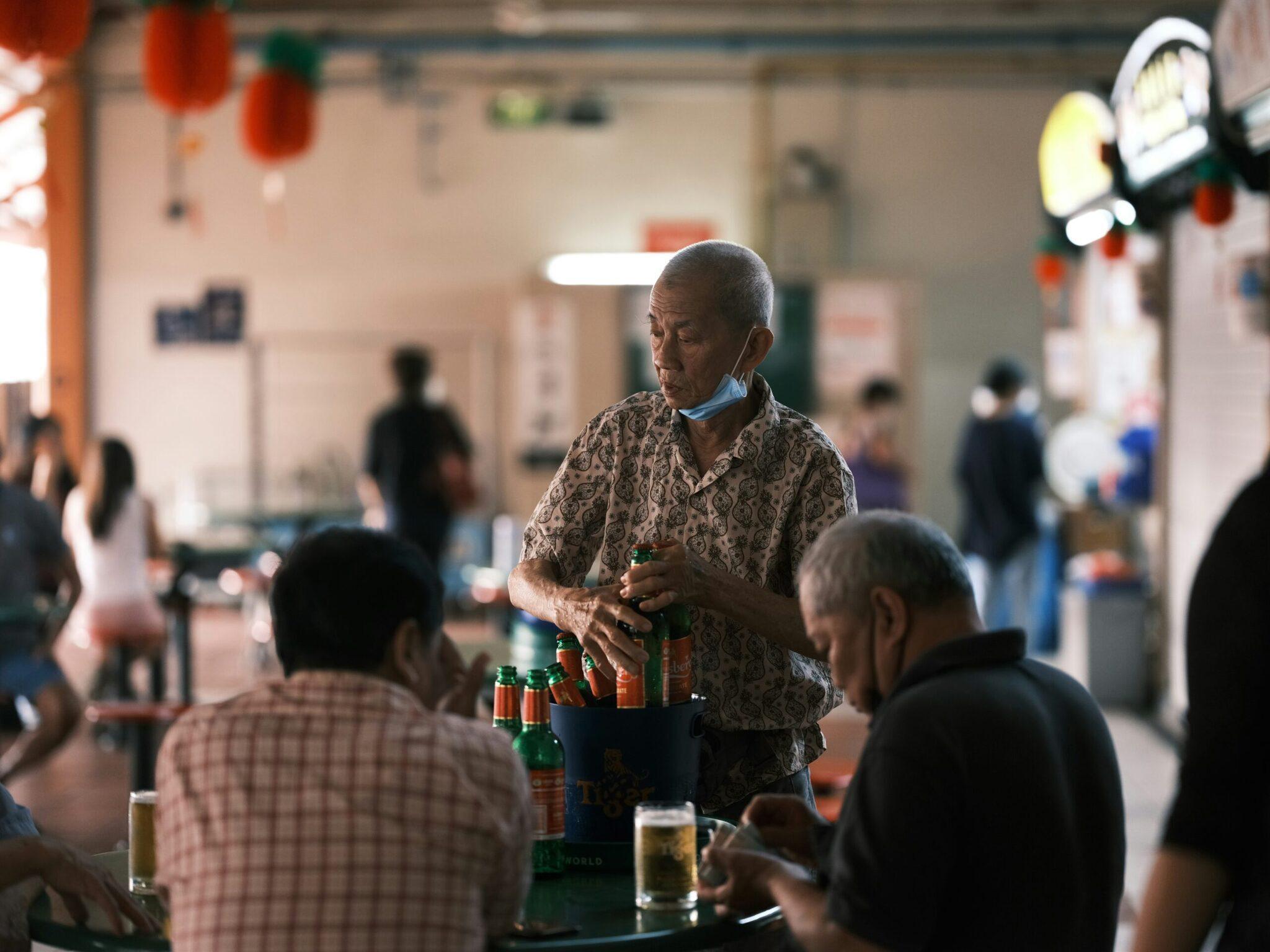 Un anziano serve birre durante una celebrazione comunitaria in una sala decorata con lanterne rosse