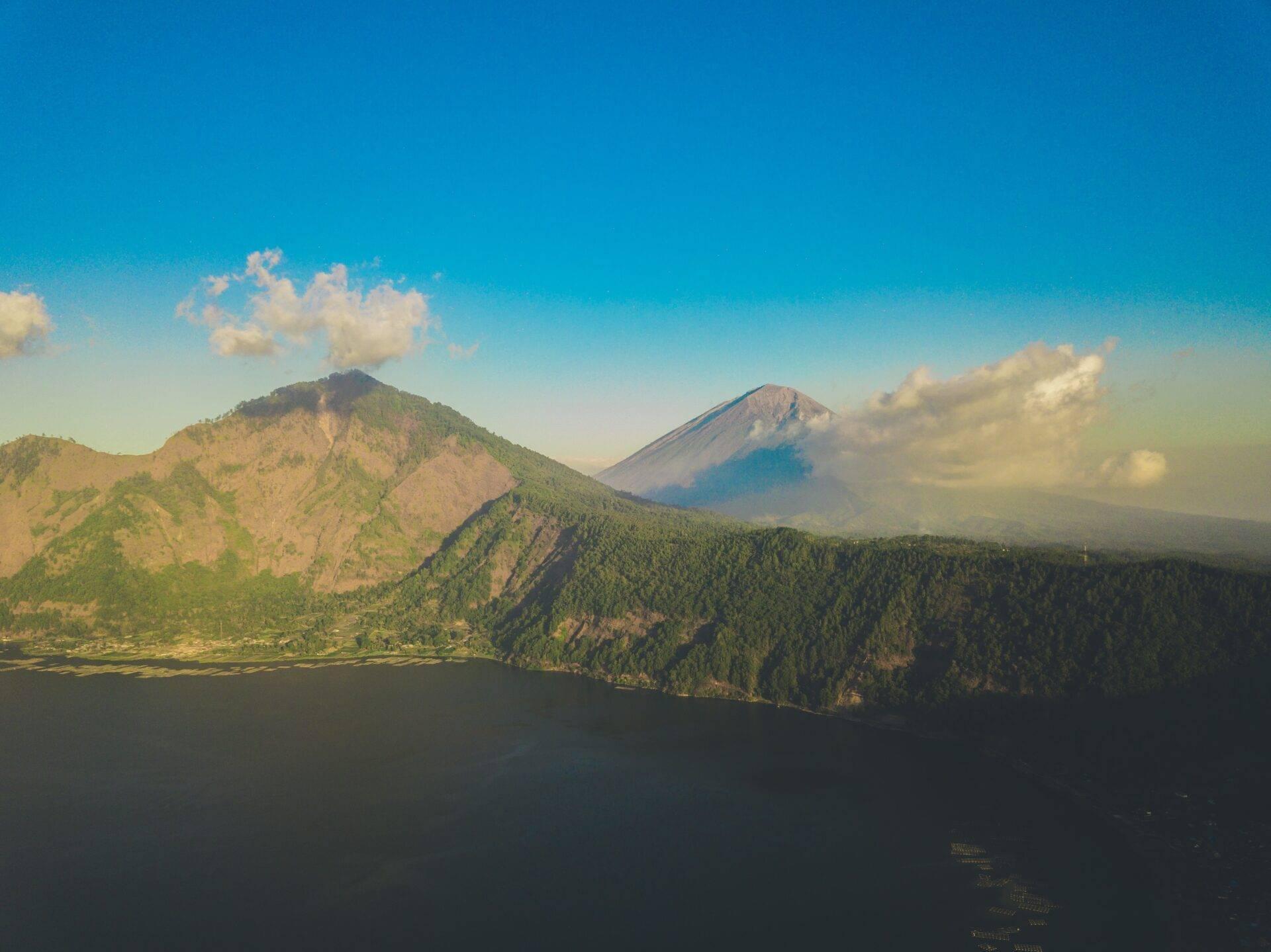Zwei bewaldete Vulkankegel spiegeln sich in einem ruhigen See unter wolkenlosem blauem Himmel