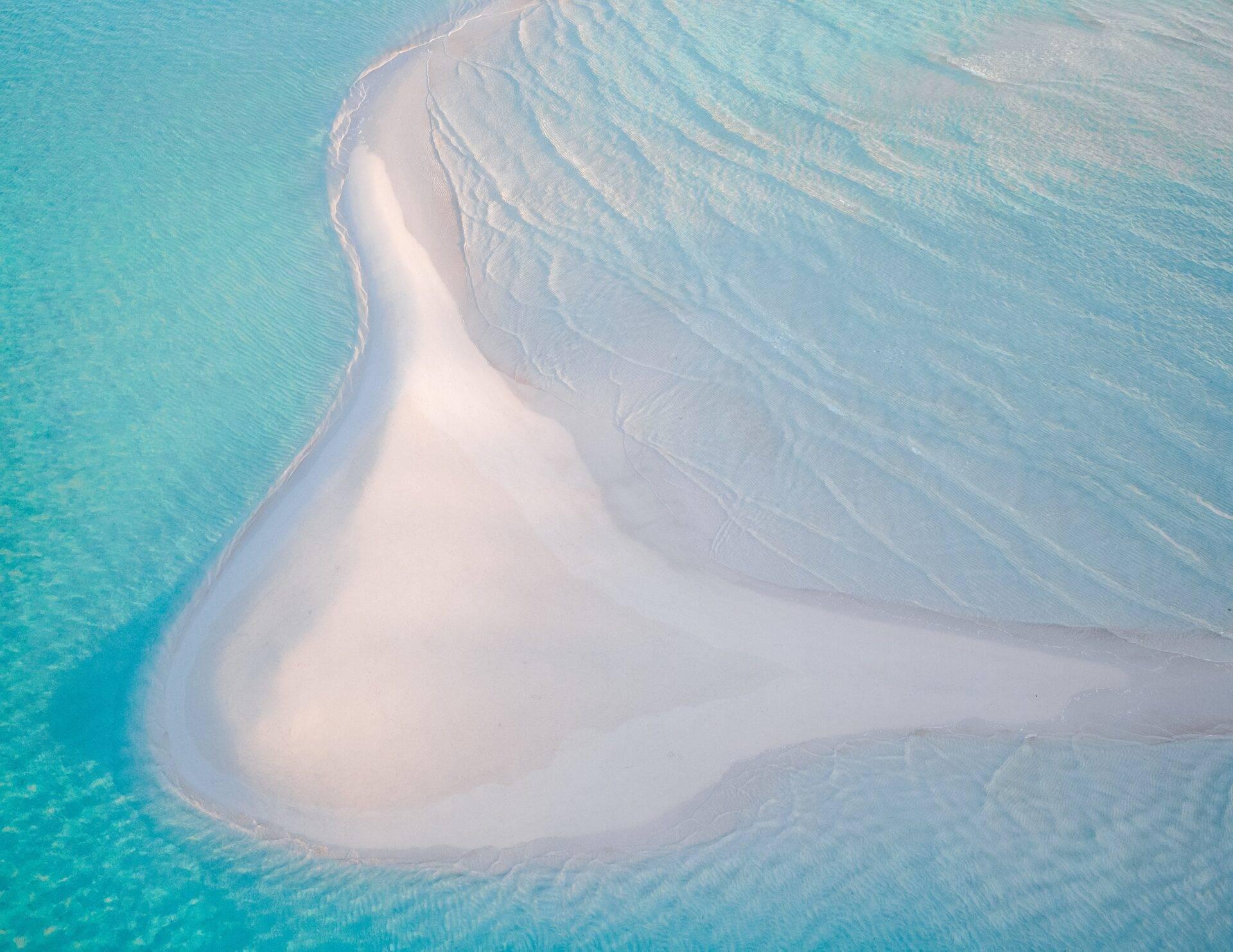 Aerial view of a crescent-shaped white sand bar surrounded by shallow turquoise waters