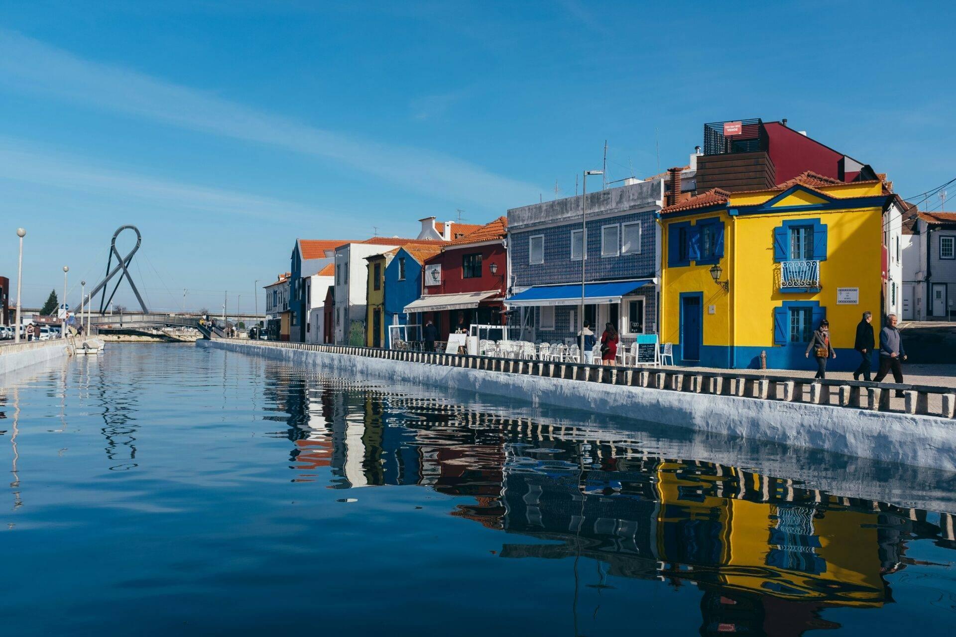 Farbenfrohe Häuser spiegeln sich in einem ruhigen Kanal einer portugiesischen Küstenstadt bei schönem Wetter