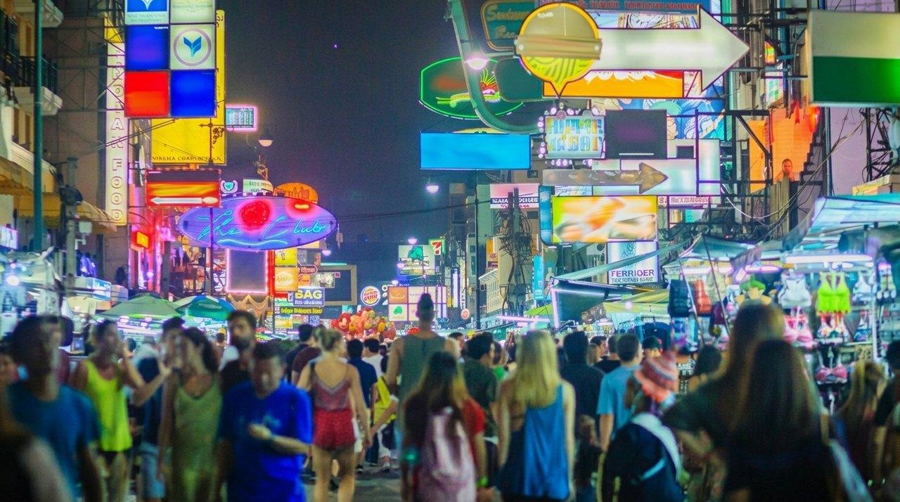 A busy commercial street at night, lit up by colourful signs and filled with tourists and passers-by