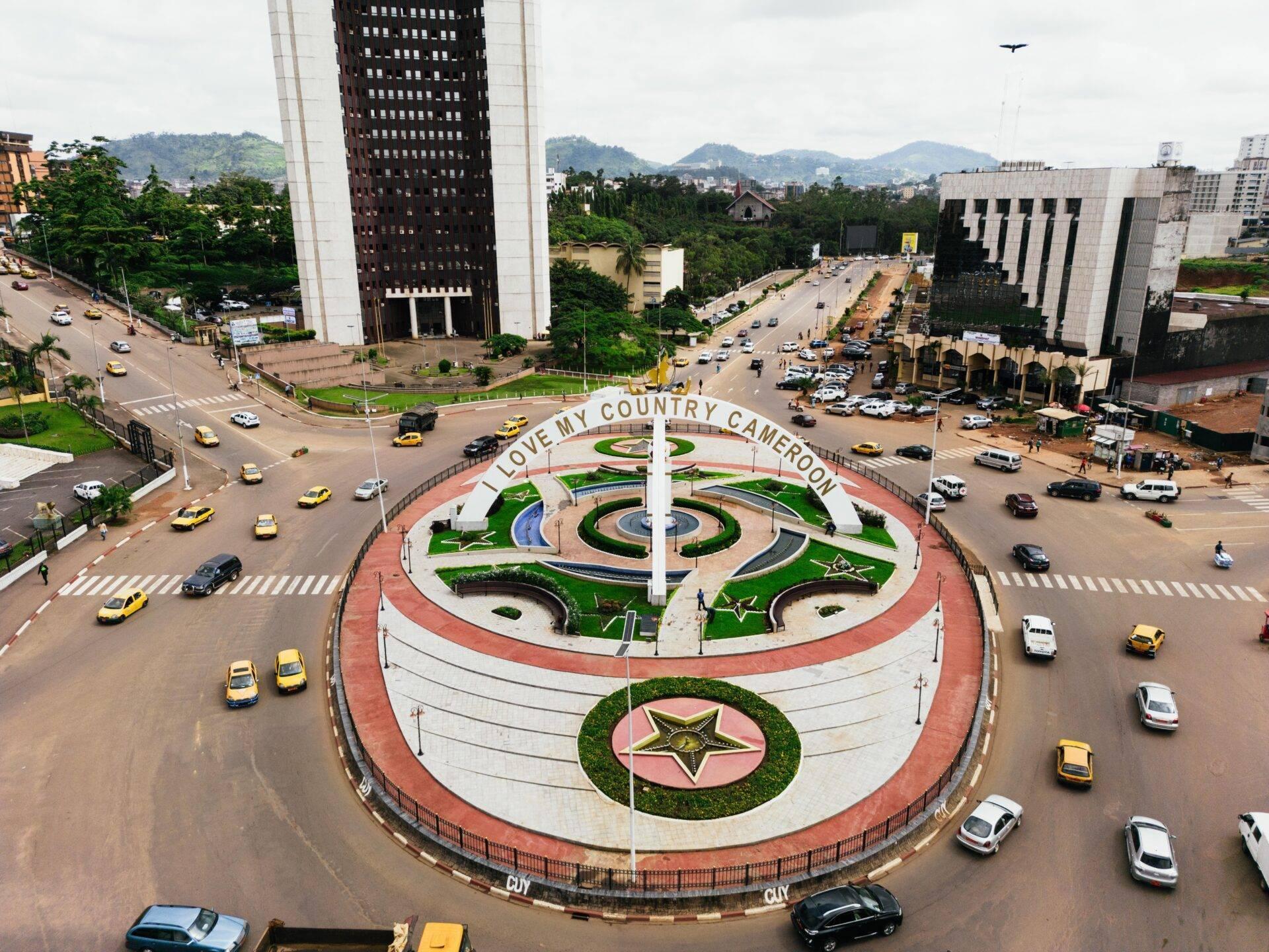 Vista aérea de una plaza circular con monumento central e inscripción patriótica, rodeada de edificios modernos y tráfico