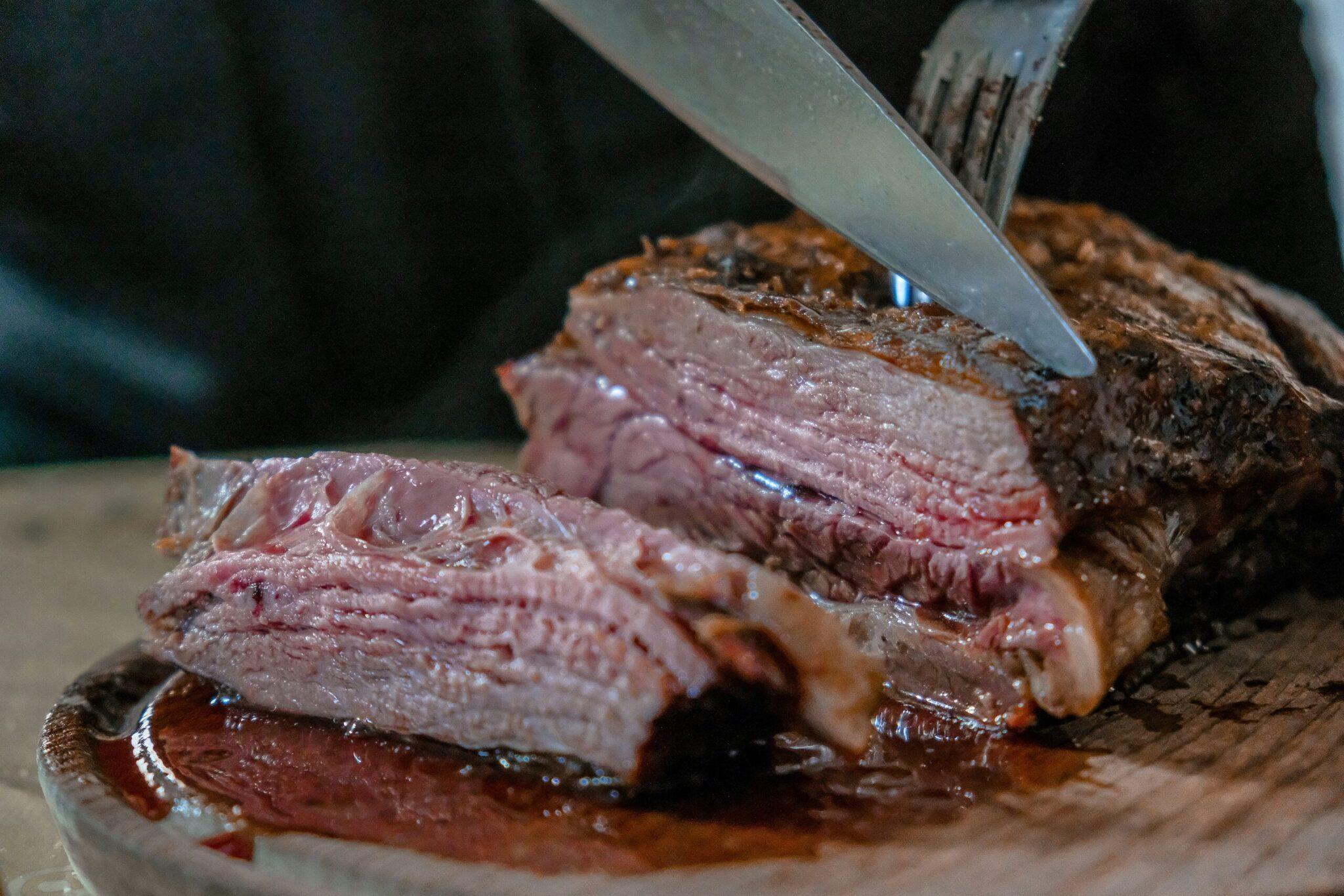 Un coltello taglia una fetta di carne rossa al sangue su un tagliere di legno, a illustrare la gastronomia locale