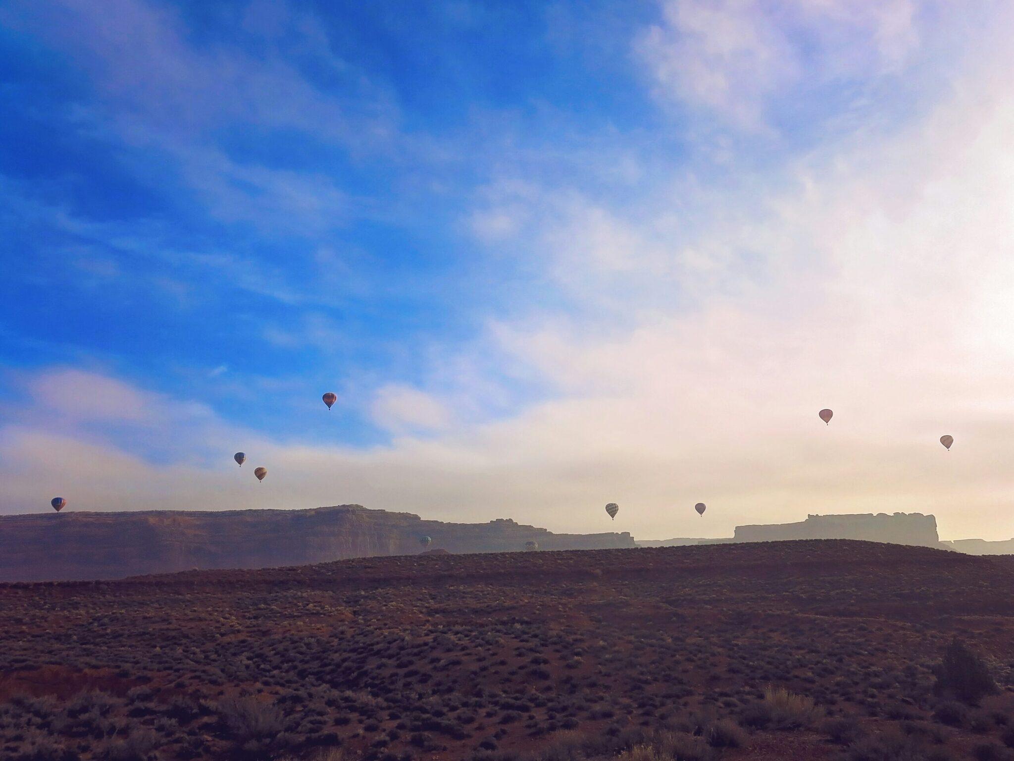 Mehrere bunte Heißluftballons schweben über einer kargen Landschaft mit Felsformationen im Hintergrund