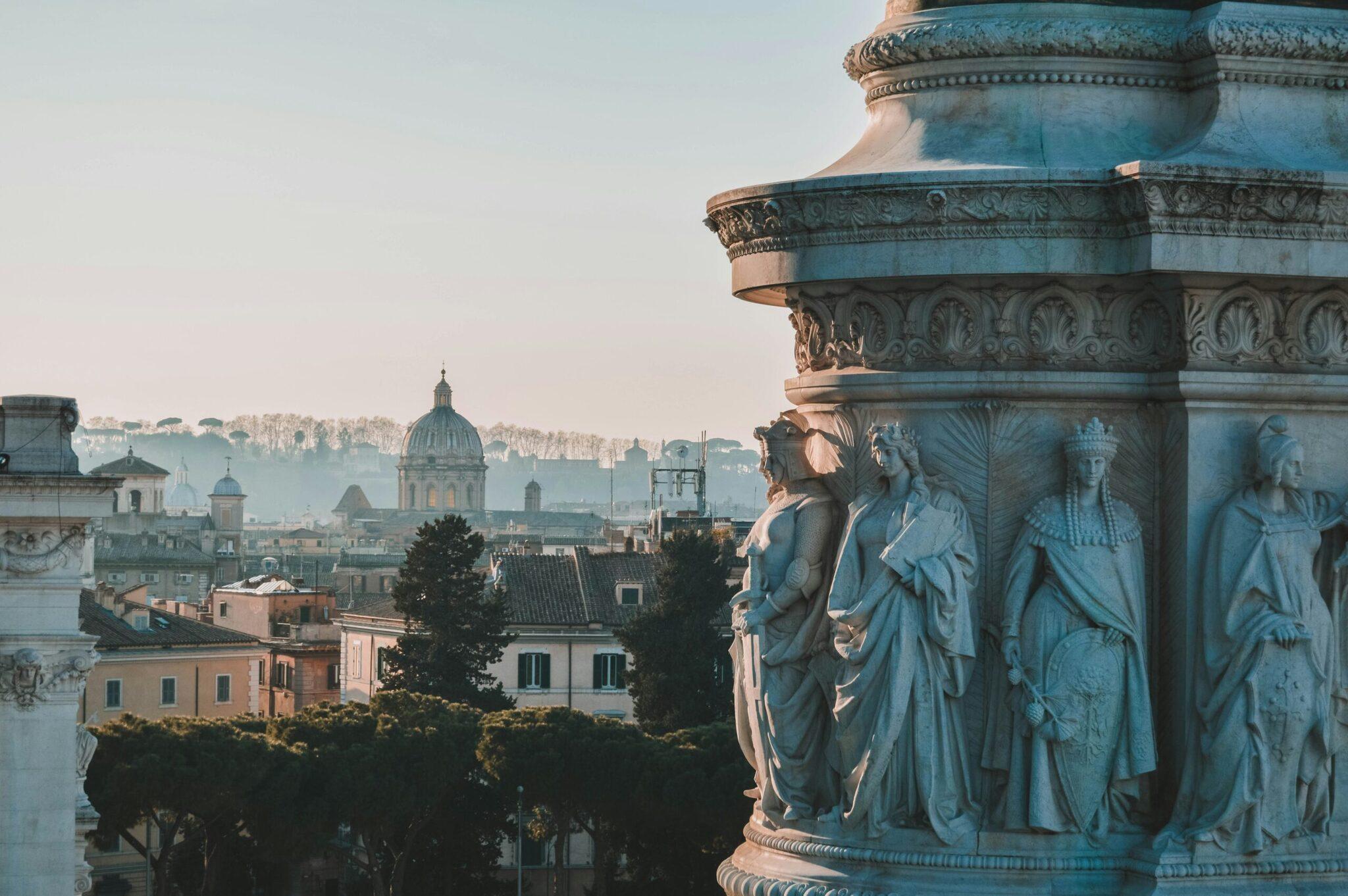 Vista panorámica de Roma con estatuas clásicas en primer plano y la cúpula de una basílica al fondo en el paisaje urbano