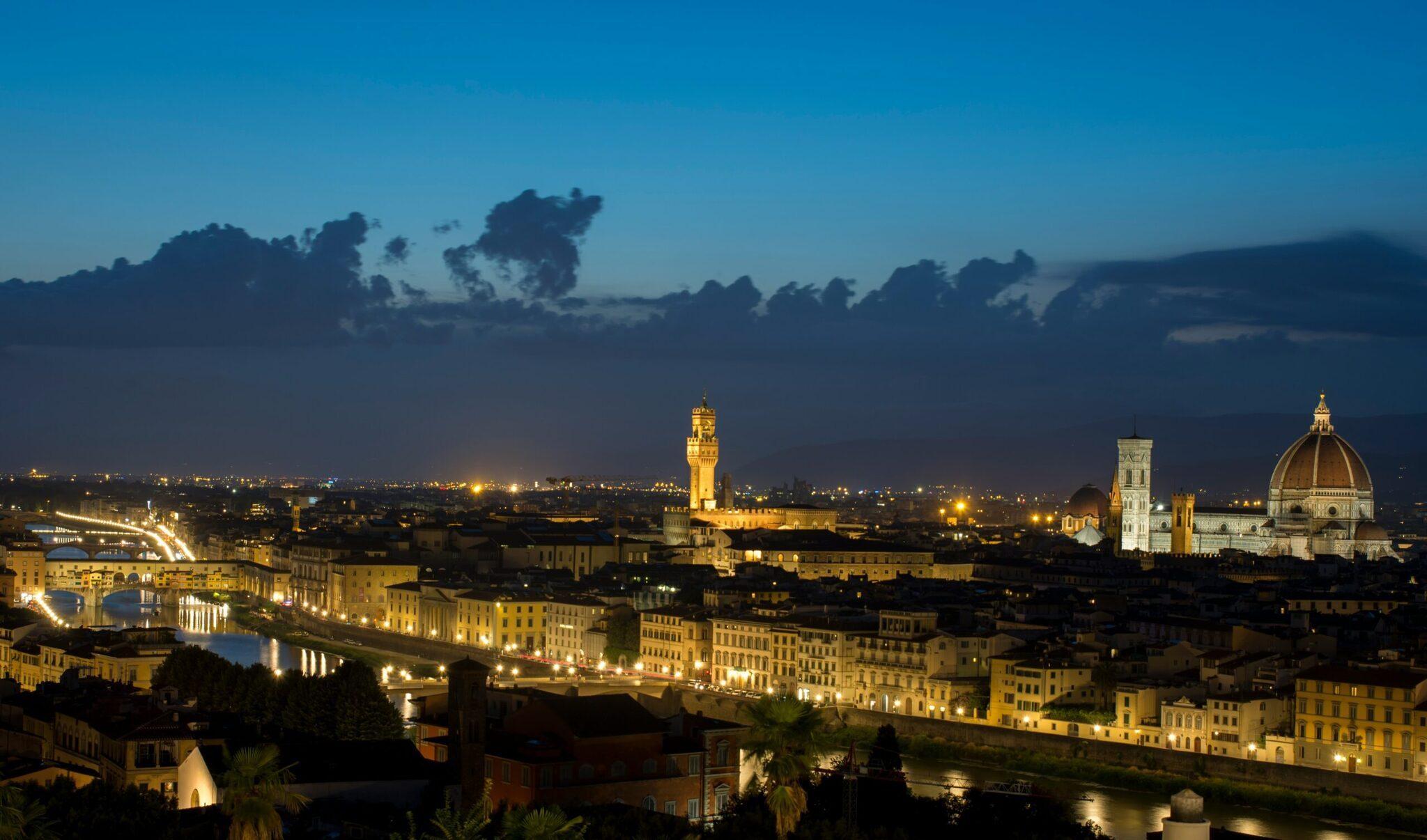 Vista nocturna de una ciudad histórica iluminada con cúpula renacentista, río y arquitectura medieval