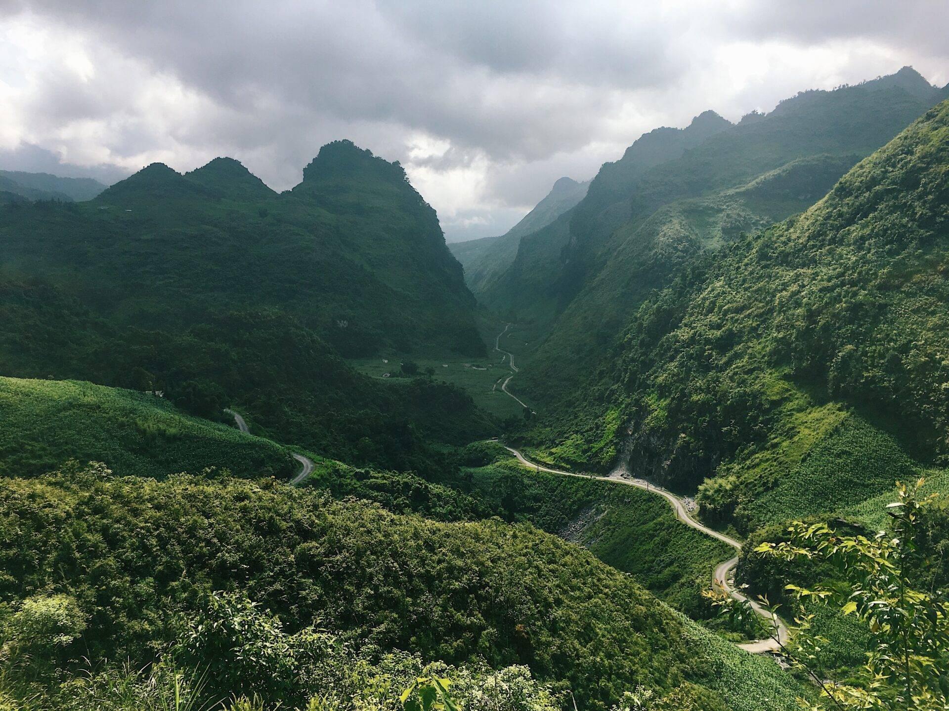 Un valle montañoso verde atravesado por una carretera sinuosa, enmarcado por picos rocosos cubiertos de jungla densa