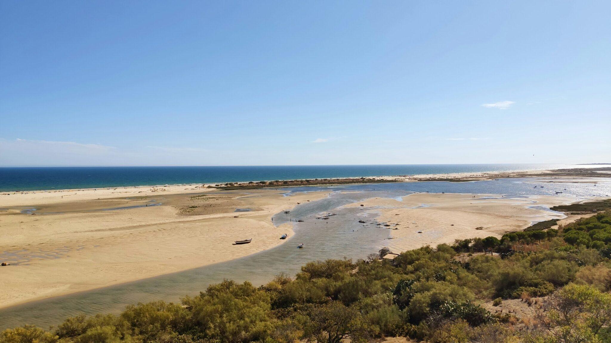Aerial view of a coastal bay with a sandy beach, turquoise water and moored boats in fine weather
