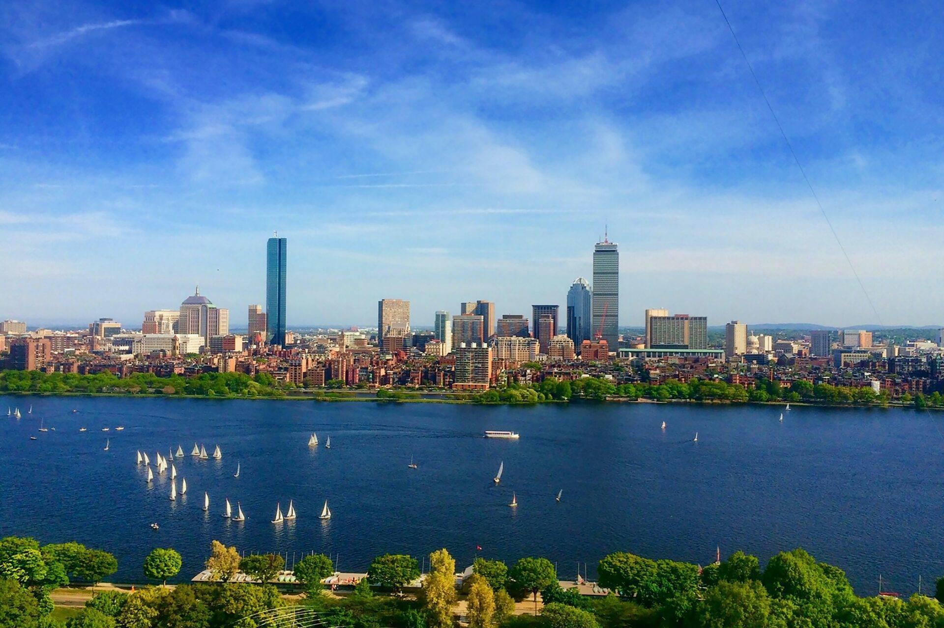 Amerikanische Stadtsilhouette mit Wolkenkratzern über einer blauen Bucht mit weißen Segelbooten und grüner Vegetation