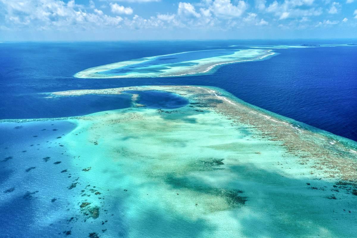 Vista aerea di atolli corallini con acque turchesi e laguna blu profondo sotto un cielo sereno