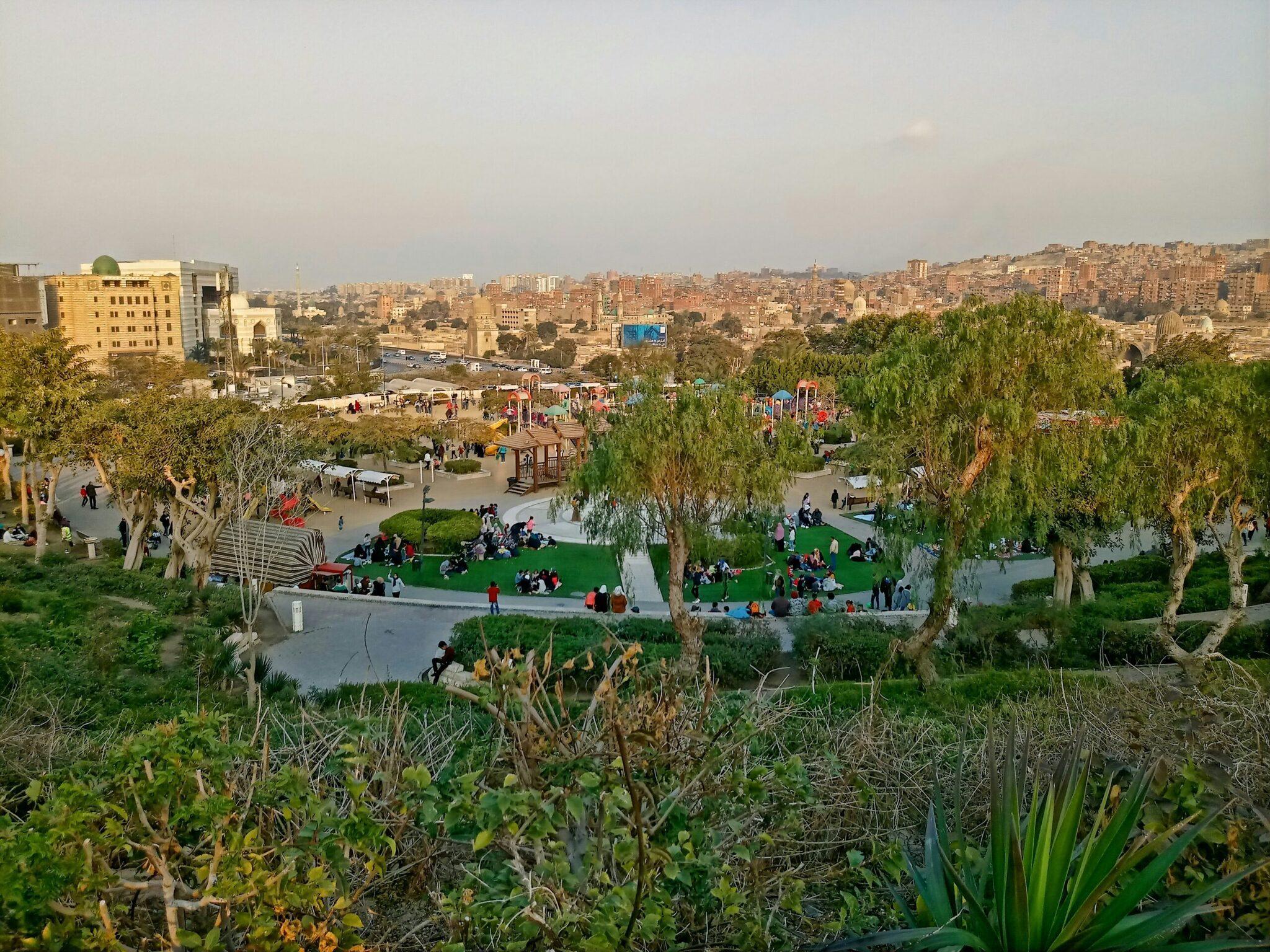 Parque urbano con zonas de juego y espacios verdes que domina una densa ciudad oriental de edificios ocres y amarillos