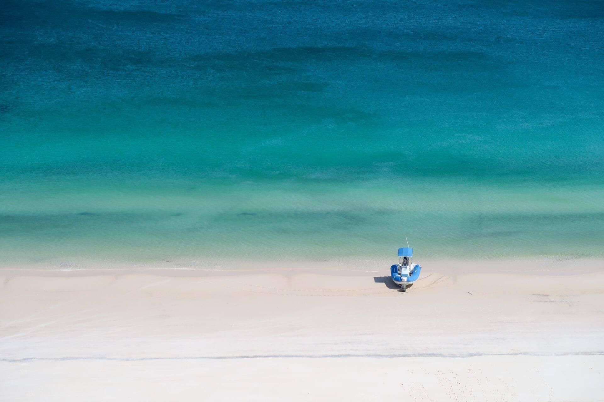 Un piccolo peschereccio blu arenato su una spiaggia di sabbia bianca di fronte a un mare turchese cristallino
