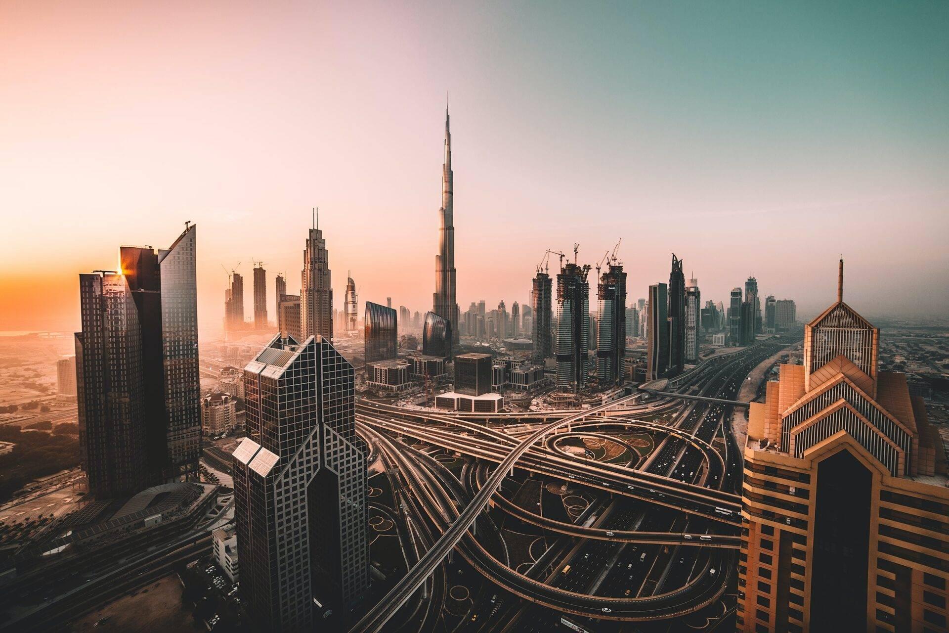 Luftaufnahme einer modernen Metropole bei Sonnenuntergang mit Hochhäusern, geschwungenen Straßen und umgebender Wüste