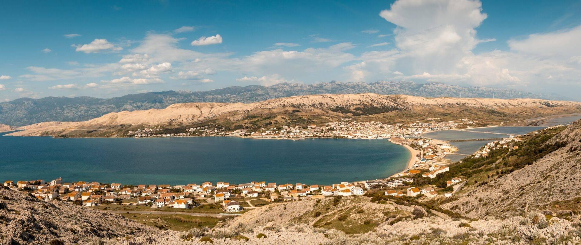 Vista panoramica di una baia mediterranea con villaggi costieri bianchi e montagna rocciosa sullo sfondo