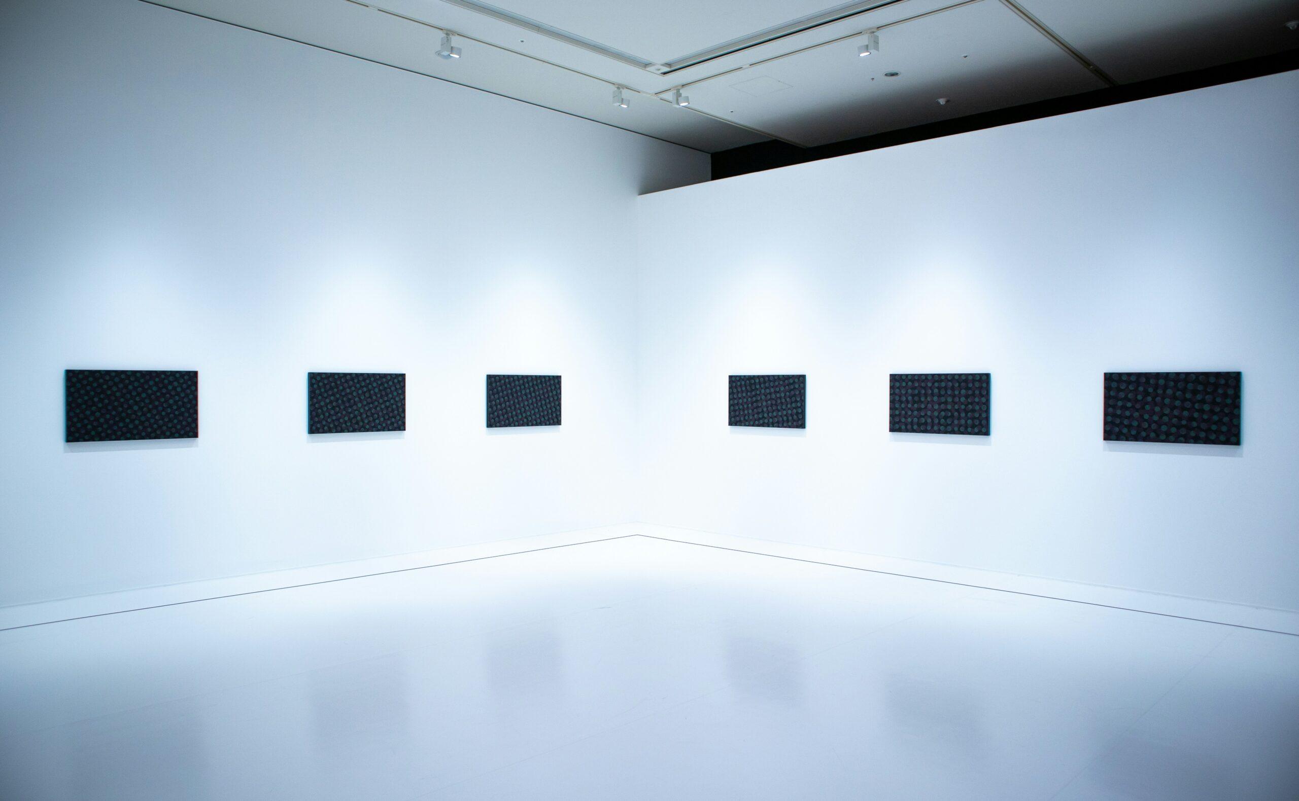 Una galleria d’arte contemporanea minimalista con sei pannelli neri disposti simmetricamente su parete bianca