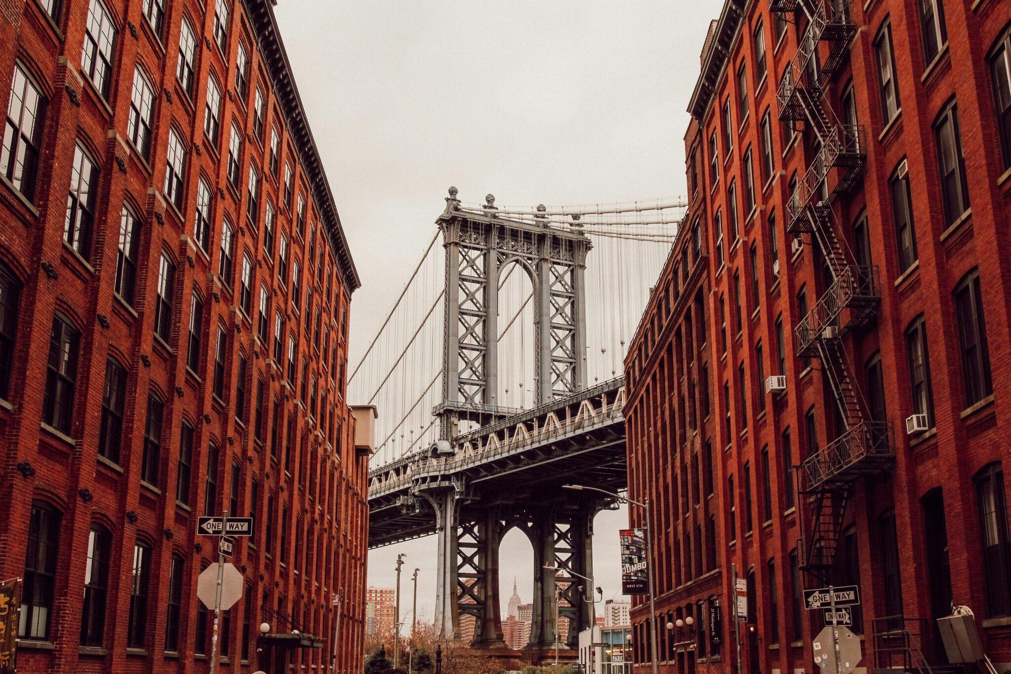 Perspective view of an elevated walkway passing between red-brick buildings in an urban setting