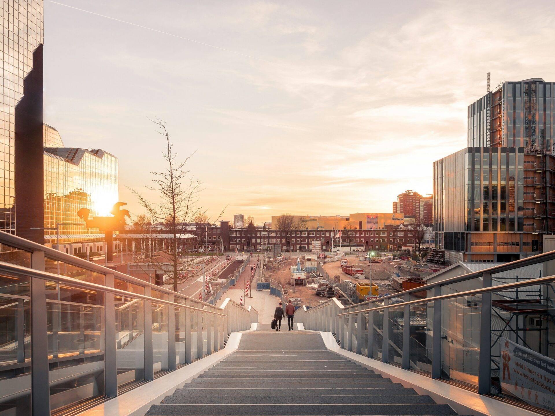 Blick von einer modernen Brücke auf eine städtische Baustelle im Wandel, mit historischen und modernen Gebäuden im Sonnenuntergang
