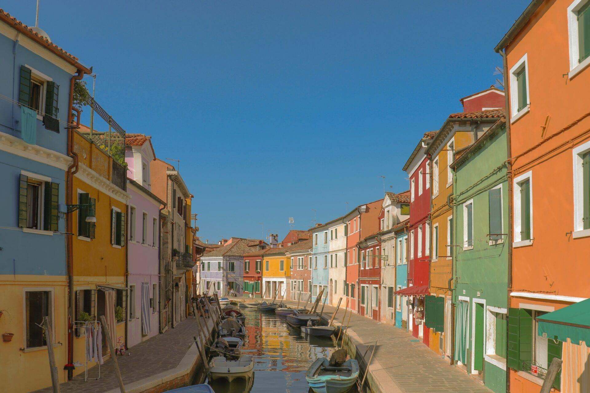 Un vicolo veneziano colorato fiancheggiato da case gialle, arancioni e verdi con barche ormeggiate nel canale