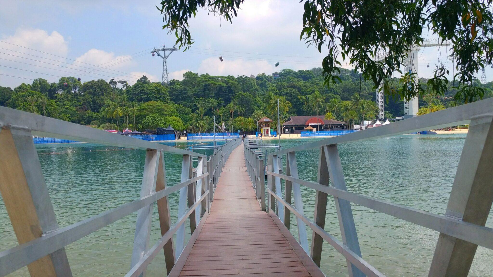 Pontile in legno che conduce a una spiaggia di laguna artificiale circondata da foresta lussureggiante e strutture moderne