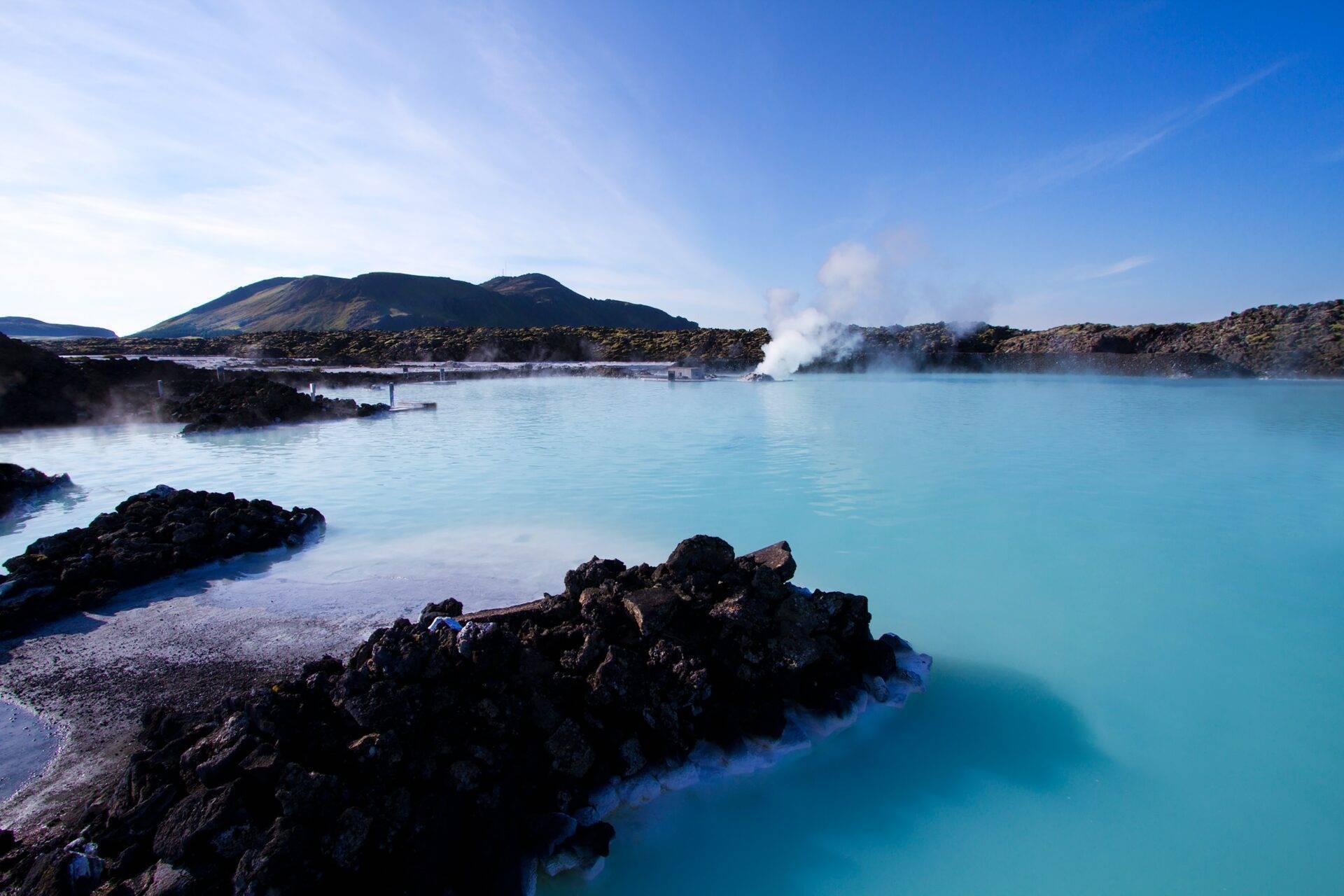 Laguna geotérmica de aguas turquesas rodeada de rocas volcánicas negras y vapores calientes