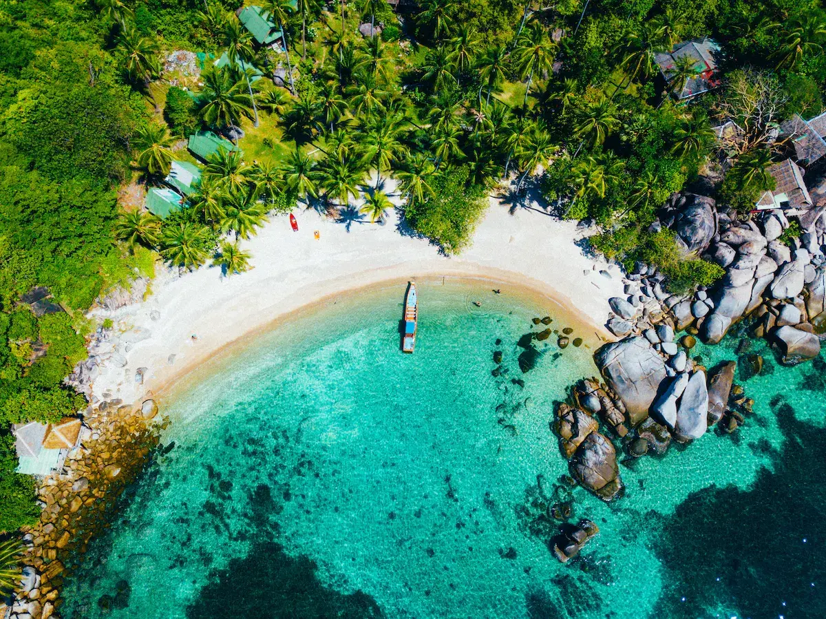 Vista aérea de una bahía tropical con playa de arena blanca, aguas turquesas cristalinas, rocas y vegetación densa