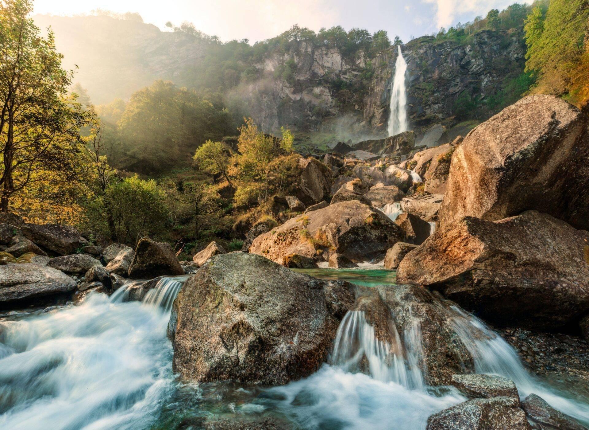 Spettacolare cascata che scorre tra pareti rocciose in una valle verdeggiante con un fiume in primo piano