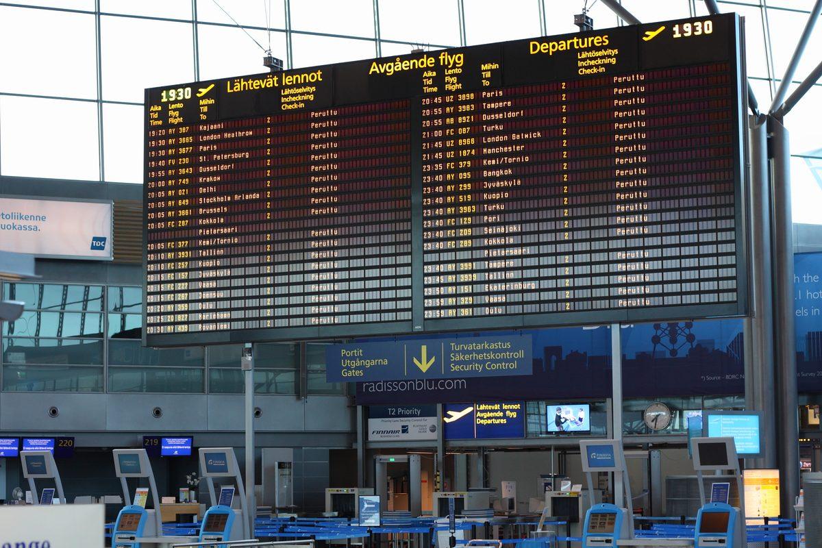 Passenger checking their phone in front of a cancelled flights departures board at an airport